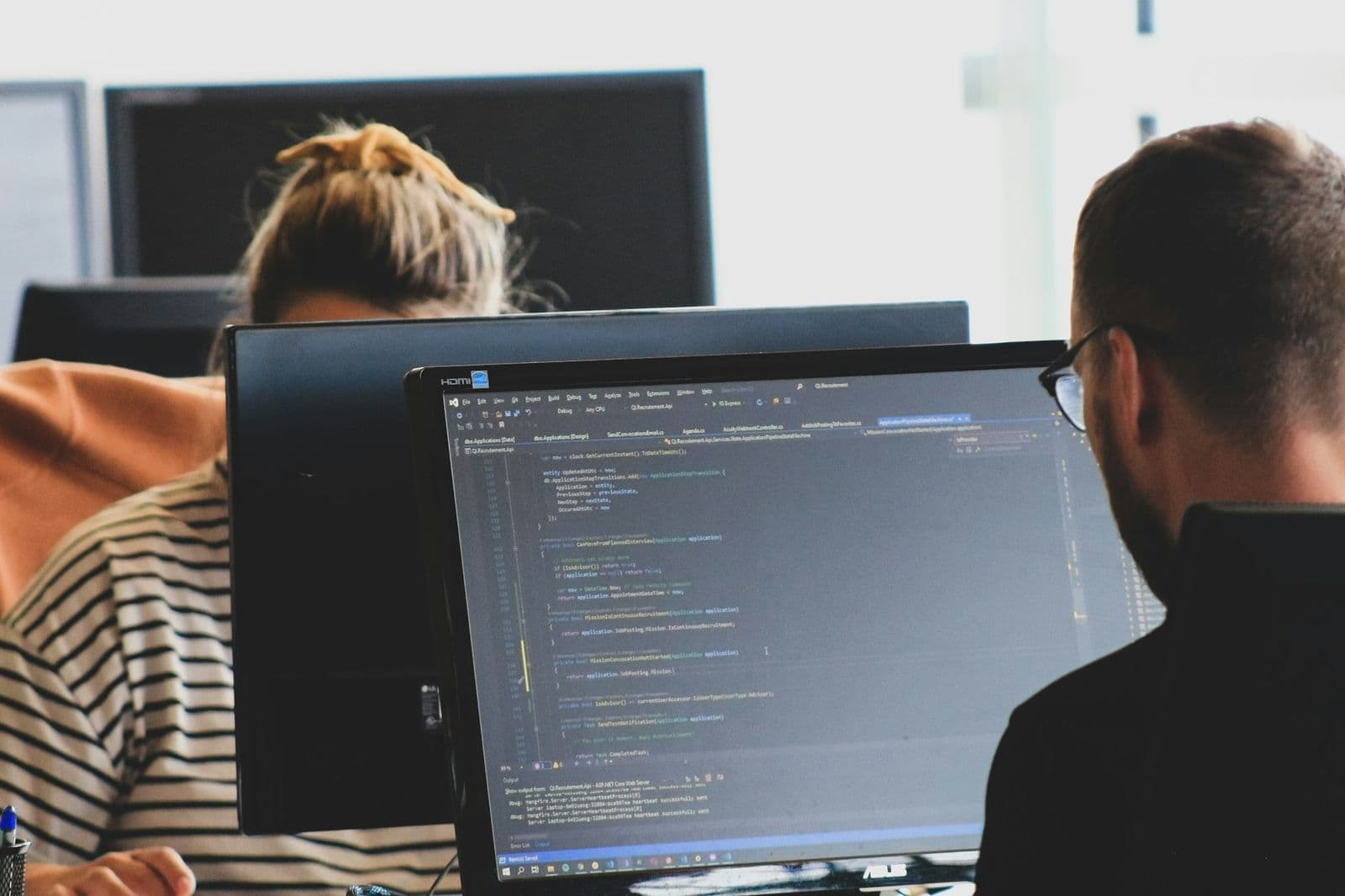 Two people seen from behind reviewing code across two monitors
